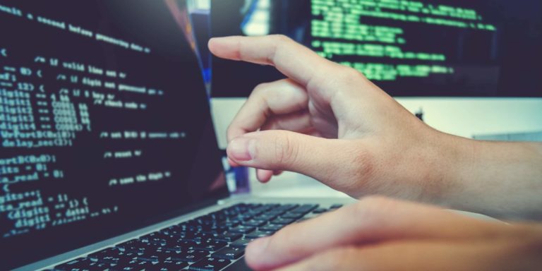 Immagine di una mano che indica una riga di codice di programmazione su un computer portatile