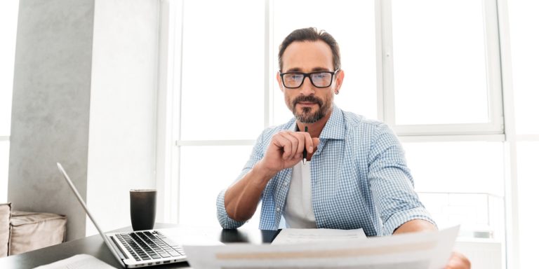Immagine di persona che guarda soddisfatta dei documenti e ha il computer portatile alla sua destra
