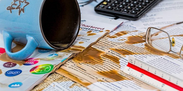 Immagine di tazza di caffè rovesciata su documenti e altri elementi da ufficio